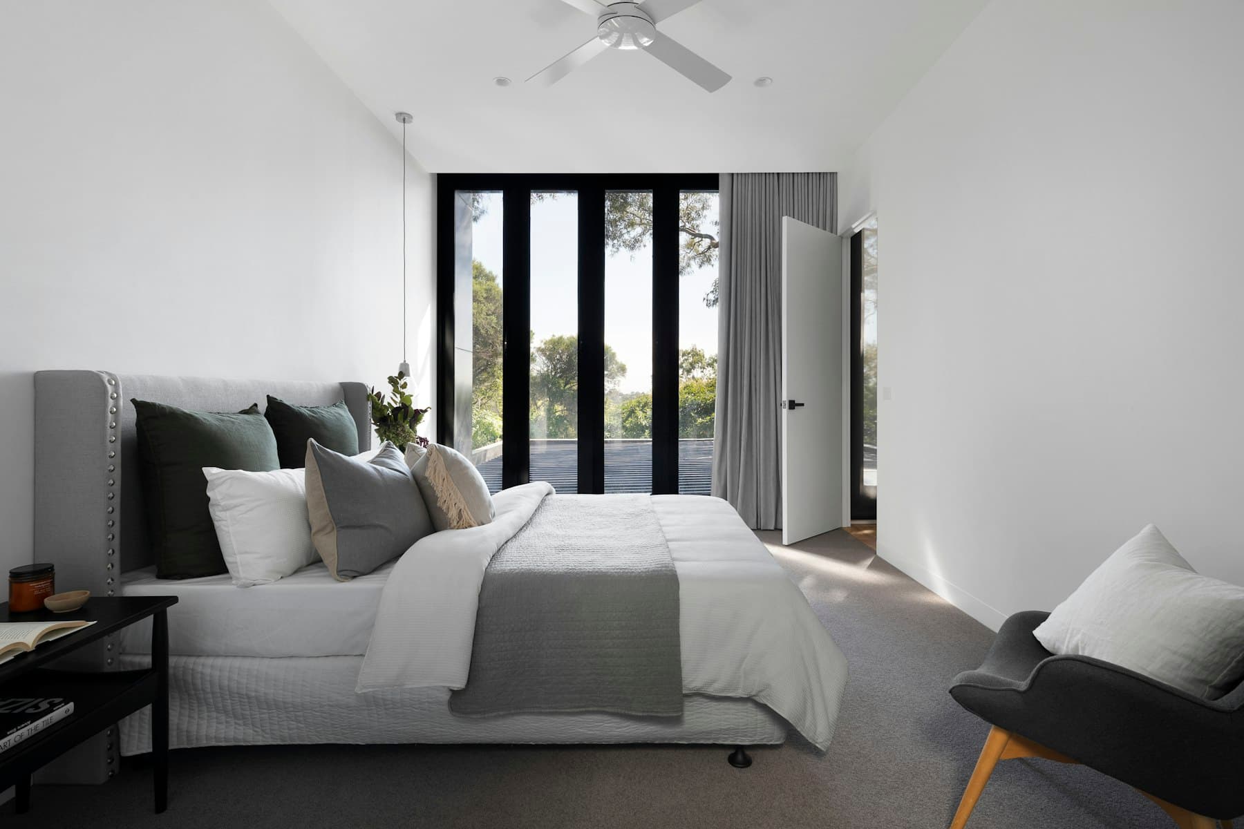 A quiet bedroom with linen bedding and trees beyond the windows.